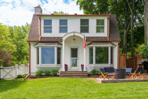 Two-story home with bay windows, front steps, and outdoor seating area in a green yard.