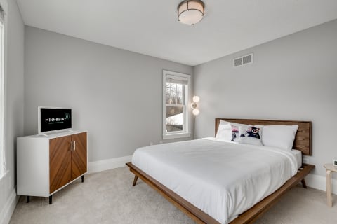 A sleek bedroom featuring a wooden bed, light gray walls, and a TV on a cabinet.
