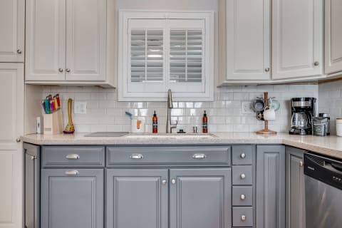 A modern kitchen featuring beige upper cabinets and gray lower cabinets with a stainless steel sink, colorful knives, and a coffee maker.