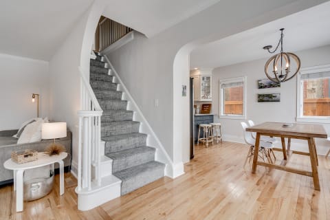 Interior of a home showcasing a staircase, gray sofa, and dining space with wooden table.