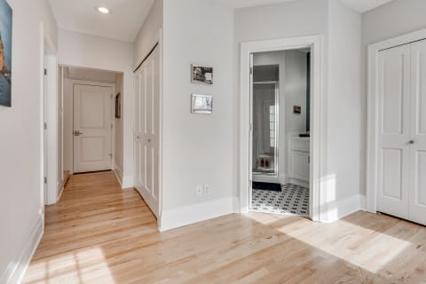 A spacious hallway with light hardwood floors and a doorway to a bathroom.