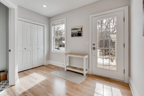 Bright entryway with wooden bench and front door, featuring large window and gray walls.