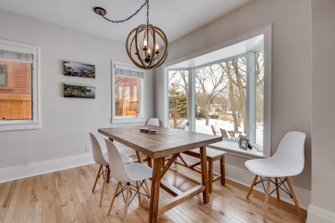 A cozy dining room featuring a wooden table, white chairs, and large windows overlooking a snowy landscape.