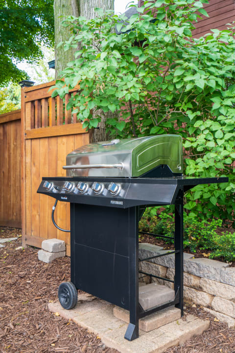 A modern black gas grill surrounded by greenery and a wooden fence.
