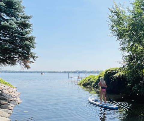 A woman on a paddleboard in a serene lake setting, with trees and a dock in the background.