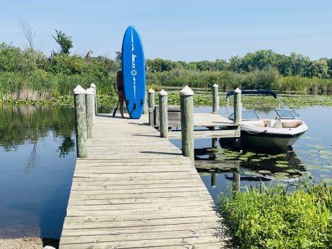 A person with a blue paddleboard walks towards a wooden dock by a lake.