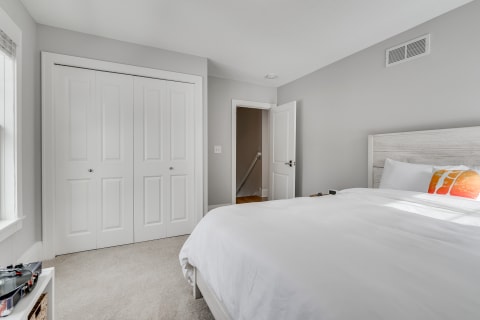 Minimalist bedroom featuring a bed with white linens, colorful pillow, and light gray walls.