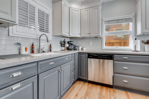 Modern kitchen with gray and white cabinetry, granite countertop, and natural light.