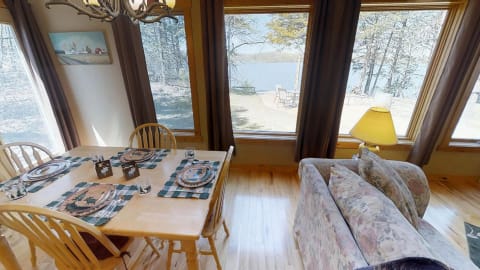 Dining area with a table set near large windows overlooking a lake.