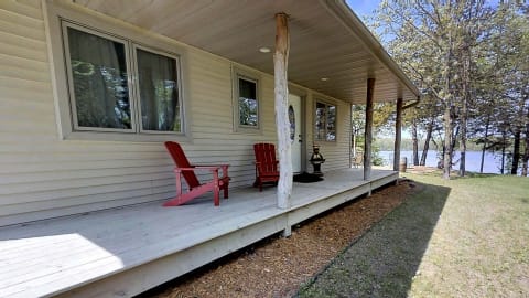 Porch of a cabin with red chairs overlooking a lake, surrounded by trees.
