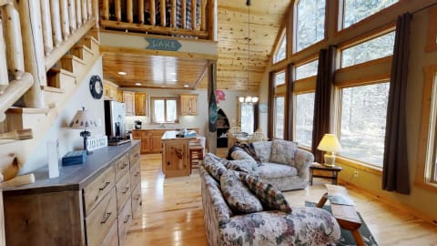 Interior of a cabin home featuring floral furniture and large windows.