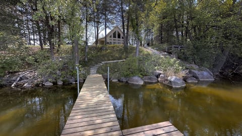 A serene lakeside view featuring a wooden dock leading to a cozy cabin surrounded by trees.