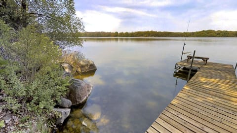 A wooden dock extending into a calm lake, with rocks and trees visible in the background.