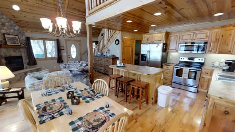 Interior view of a rustic kitchen and living room with wooden accents and stone fireplace.
