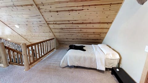 Cozy loft bedroom with wooden beams, plush bed, and soft carpet.