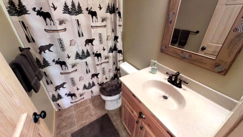 A cozy rustic bathroom with a woodland-themed shower curtain and natural decor.