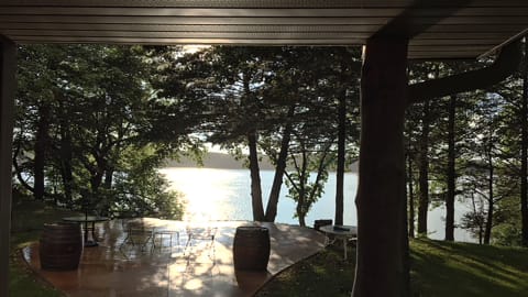 View from a covered patio overlooking a lake, with furniture and trees in the foreground.