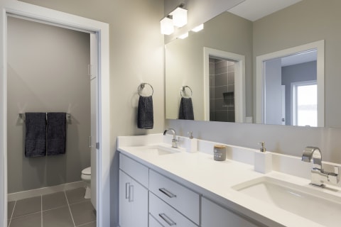 Modern bathroom with double vanity, gray tiles, and elegant light fixtures.