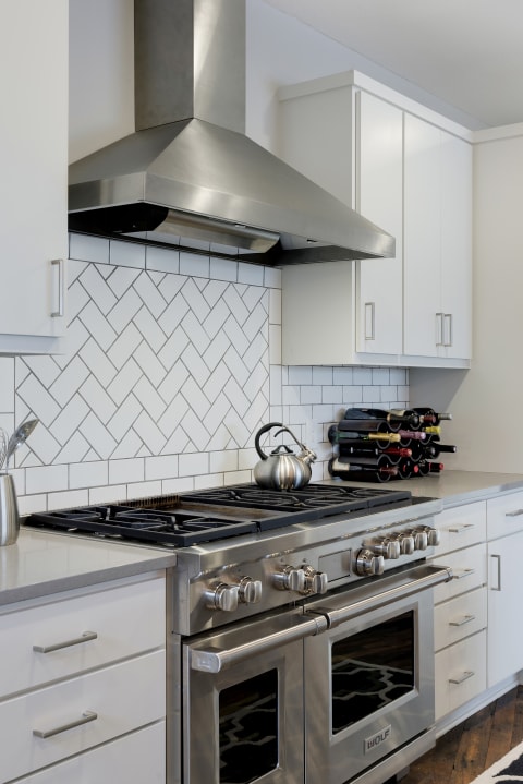 Modern kitchen with stainless steel stove, herringbone tile backsplash, and wine storage.