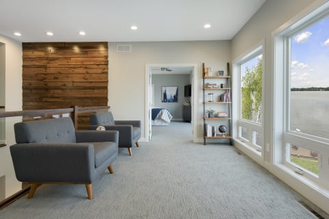 Living room featuring gray armchairs, a wooden accent wall, and large windows with a lake view.
