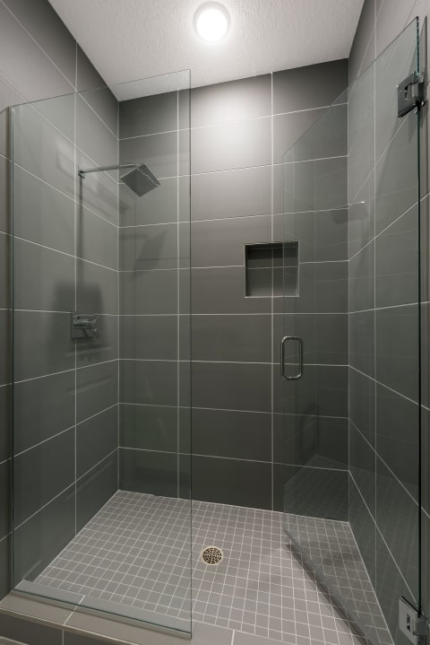 Modern shower with glass doors and gray tile walls.
