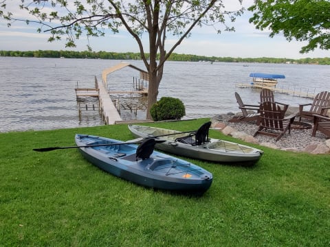 Kayaks on green grass next to a wooden dock on a lake.
