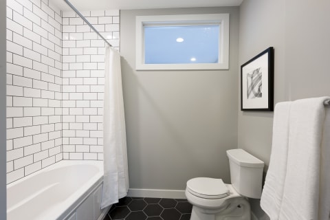 A sleek modern bathroom showcasing a white tub, black hexagonal floor tiles, and framed artwork.