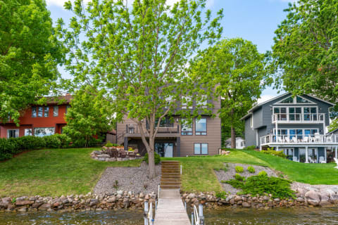 A view of modern lakeside homes with a wooden dock and greenery.