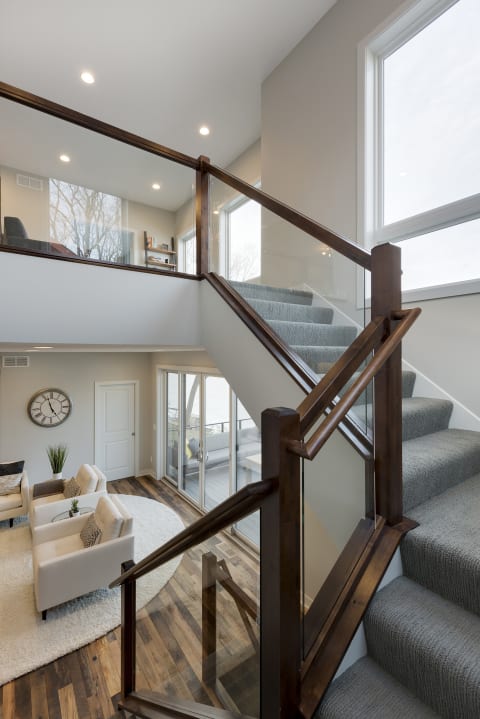 An elegant staircase with carpeted steps and a glass railing, overlooking a stylish living area.