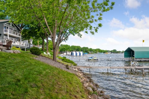 A serene lakeside view featuring a home, trees, and docks with colorful canopies.