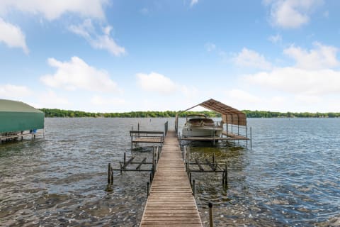Lakeside dock with a motorboat covered by a canopy and lush green trees in the background.