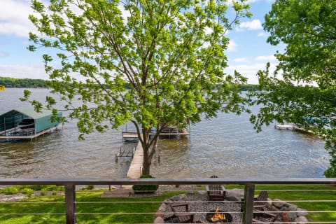 Lakeside view with a fire pit, green trees, and wooden docks.