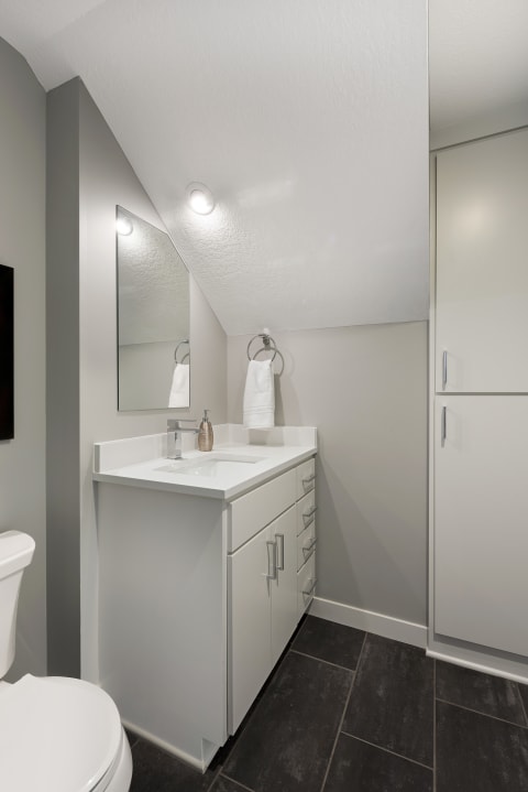 Modern bathroom with a white vanity, gray walls, and dark tile flooring.