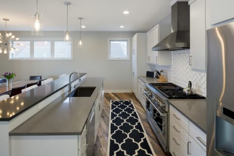 Contemporary kitchen with white cabinets and grey countertop, featuring stylish pendant lights and a dining table in the background.