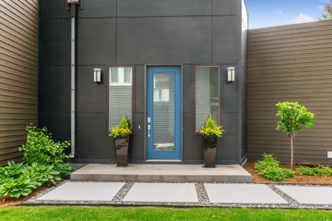 A contemporary house entrance with a blue door and planters filled with flowers.