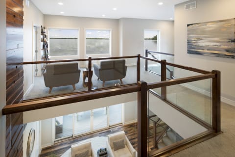A spacious loft area featuring grey armchairs and a view of the waterfront through large windows.