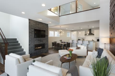 A contemporary living room with white sofas, a stone fireplace, and a dining area in an open plan layout.