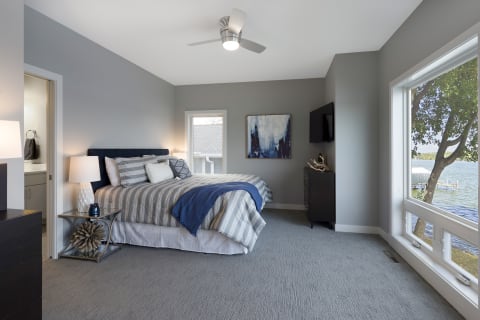 Modern bedroom with lake view, featuring gray walls and a well-made bed.