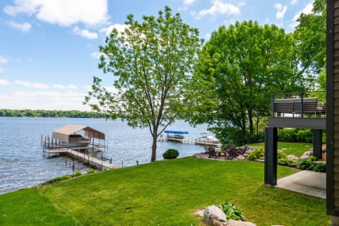 Lakeside view featuring a green lawn, dock, boat lift, and Adirondack chairs near a fire pit.