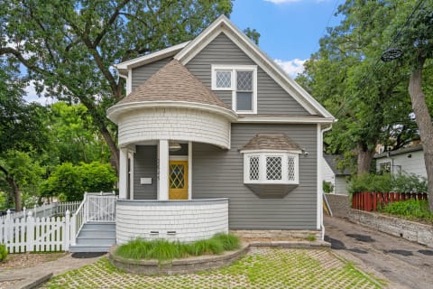 A two-story house with a rounded turret, gray siding, and a vibrant yellow door.