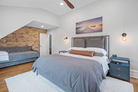 A modern bedroom featuring a king-sized bed, a gray tufted couch, and exposed brick walls.