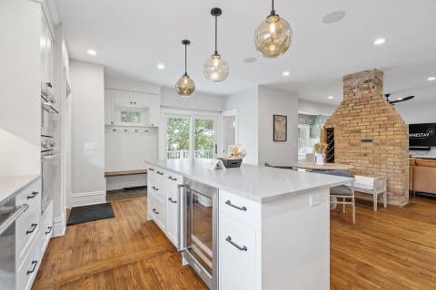 Modern kitchen featuring a spacious island, pendant lighting, and a rustic brick chimney.