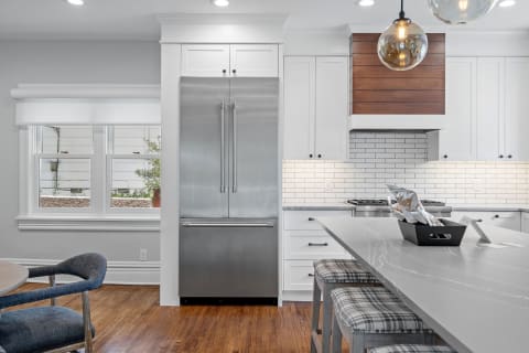 Modern kitchen with stainless steel refrigerator, white cabinetry, and a gray countertop island.
