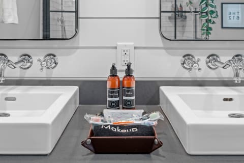 A contemporary bathroom counter with two sinks, amber soap bottles, and makeup items.