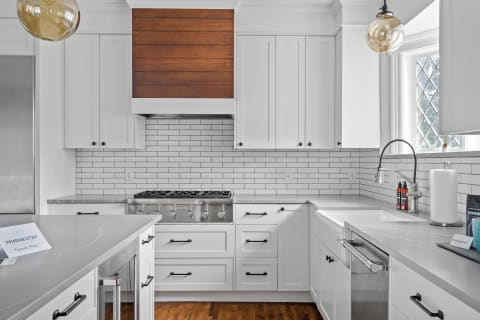 A contemporary kitchen with white cabinetry, a wooden accent wall, and stainless steel appliances.