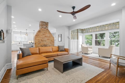 Modern living room featuring a leather sofa, brick fireplace, and large windows.