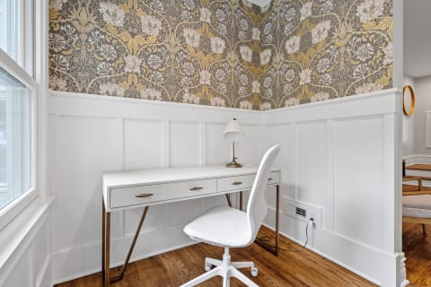 Corner office arrangement with a white desk, chair, and floral wallpaper.