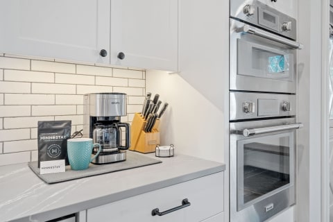 A contemporary kitchen countertop with a KRUPS coffee maker, a blue mug, a coffee bag, and a knife block.