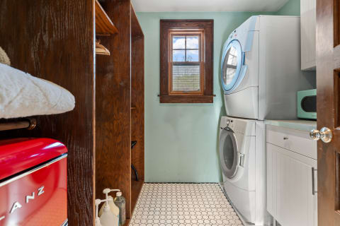 A laundry room featuring a stacked washer and dryer, dark wooden shelves, and mint green walls.