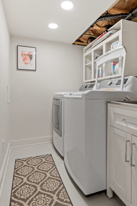 A bright and tidy laundry room with a washing machine, dryer, shelf, and decorative rug.